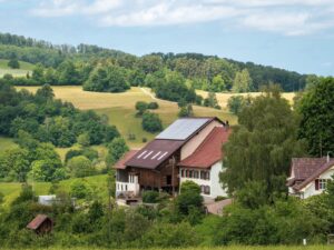 Villa med solceller omgiven av gröna fält och skog.